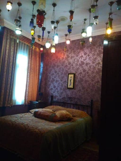 Bedroom at Kybele Hotel featuring patterned wallpaper, a double bed with decorative pillows, thick curtains, and colorful hanging lamps—showcasing the unique charm of this boutique Istanbul hotel.