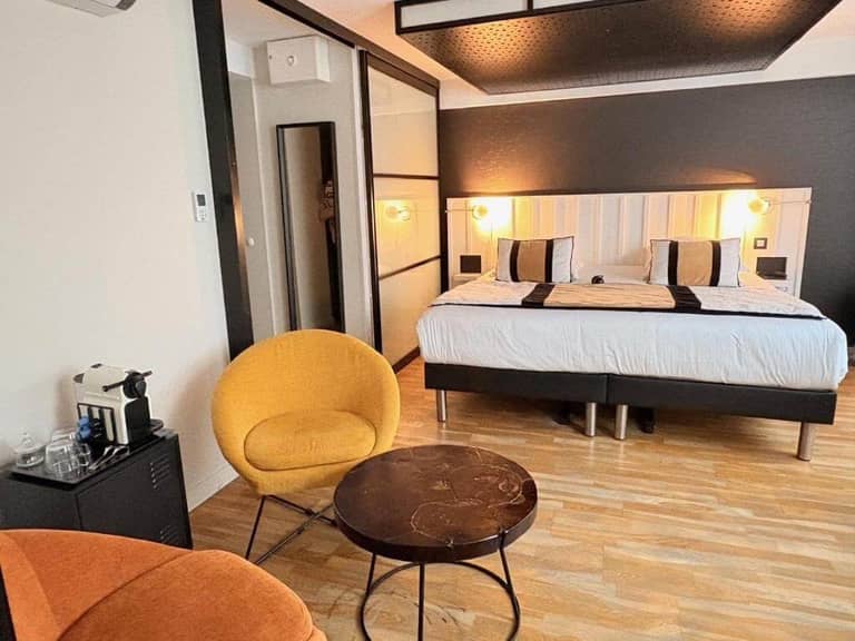 Modern hotel room in La Rochelle with a double bed, two round yellow chairs, a small dark fabrique table, wood flooring, and a coffee machine on a side table.