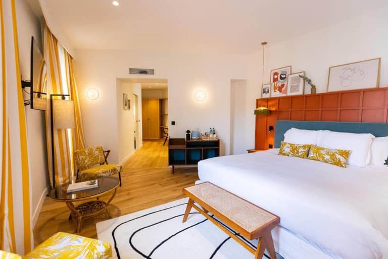 Hotel Durante offers a bright, airy room with a large bed, yellow-patterned armchairs, a small table, desk, and modern decor. Wooden flooring and striped curtains add charm to this nice hotel’s inviting space.