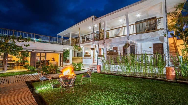 A two-story white building with balconies and outdoor lighting, Hotel Terasu Salento features a grassy courtyard with chairs around a lit fire pit at night.