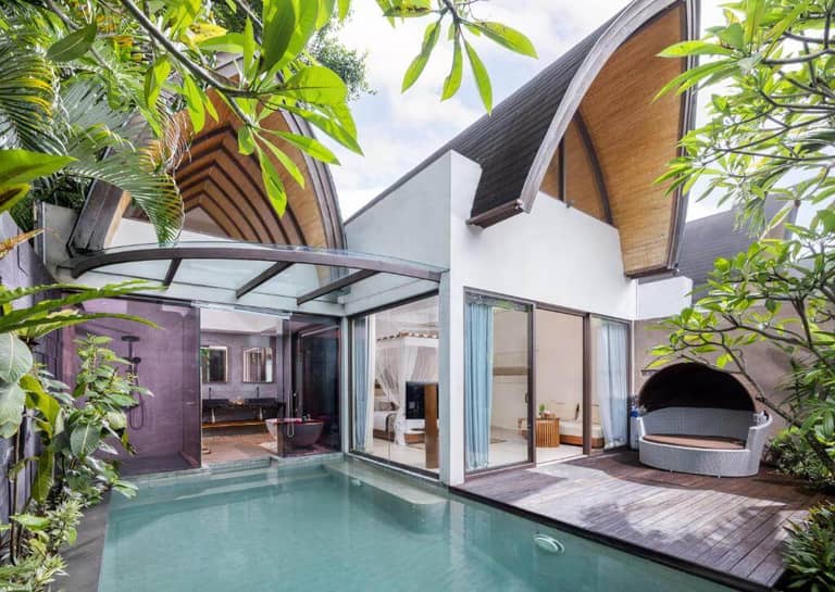 Modern Lalasa Villas in Canggu feature a private pool, outdoor shower, glass doors, wooden deck, and lush green plants; curved wooden roofs add architectural interest.