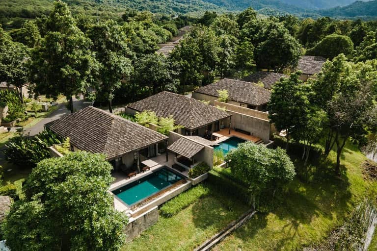 Aerial view of modern villas with private pools at MUTHI MAYA Resort Khao Yai, surrounded by lush greenery and trees, set against a backdrop of forested hills in beautiful Khao Yai.