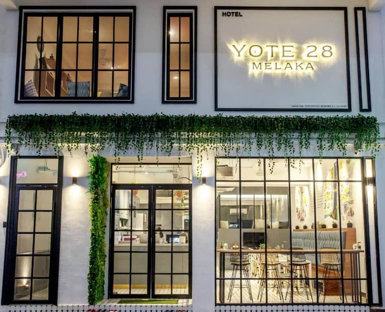 Exterior view of Yote 28 Melaka hotel with large windows, greenery above the entrance, and a visible seating area inside welcomes guests to the stylish Yote 28 Melaka experience.