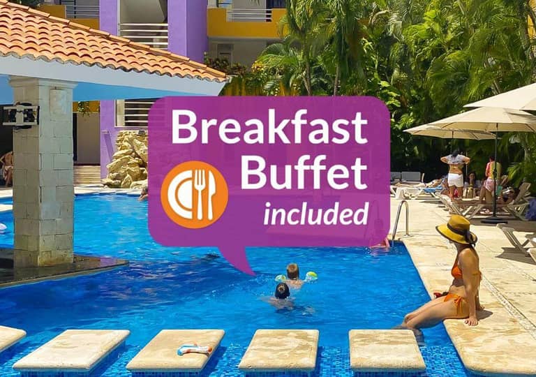 A woman relaxes by the Adhara Hacienda Cancun resort pool while two children swim; a sign reads “Breakfast Buffet included” with a plate and utensils icon, capturing a perfect family moment in Cancun.